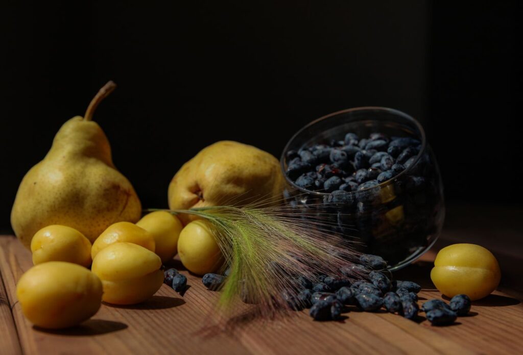 Vivid still life showcasing pears, yellow plums, and blueberries on a wooden surface.